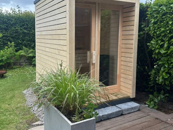 Moderne Außensauna INA Seitenansicht im Garten mit Glasfront